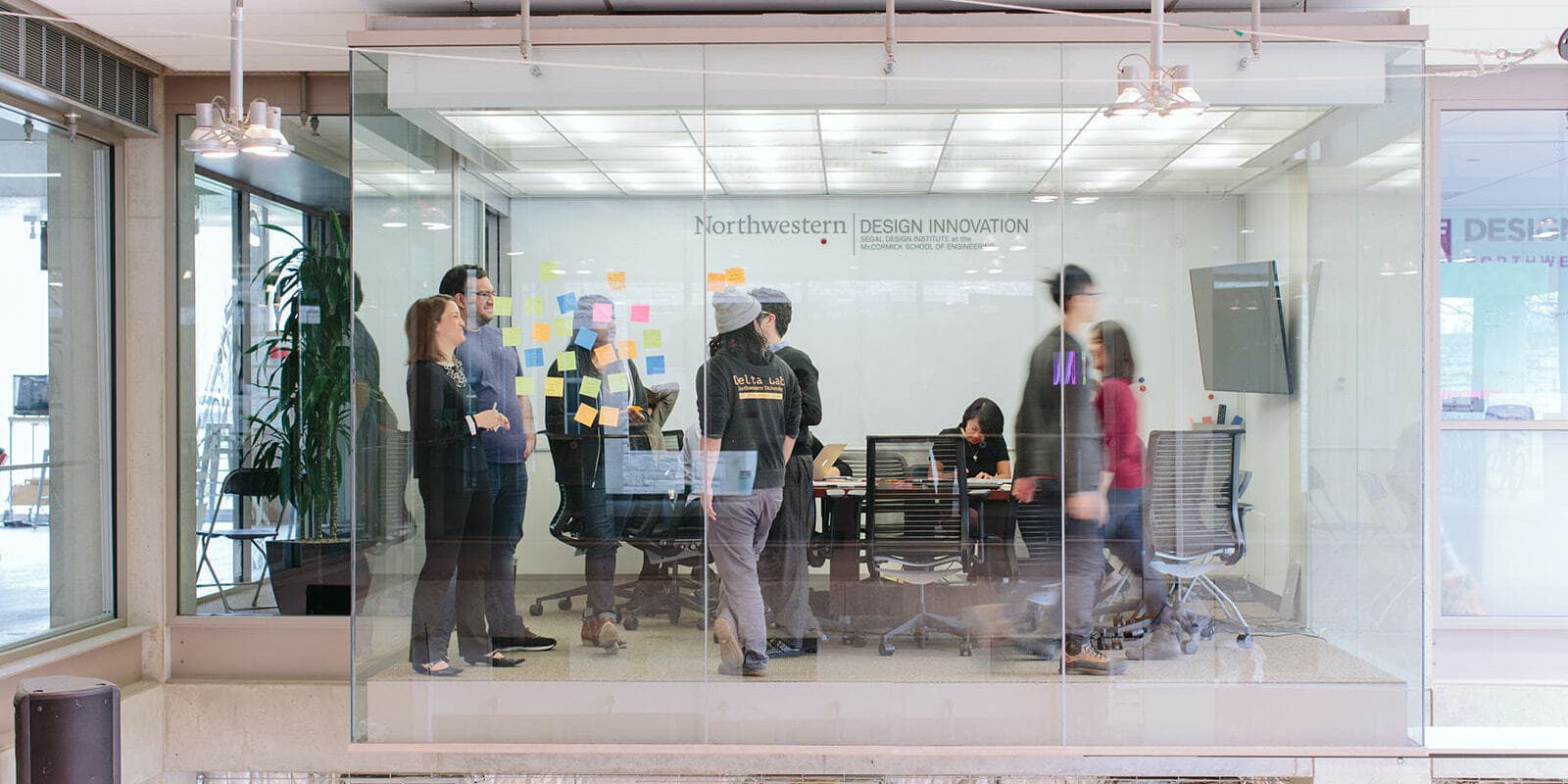Lab members collaborating with post-it notes in a glass fishbowl-like room.